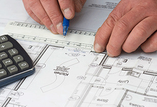 Builder measuring a building drawing with a scale rule and calculator